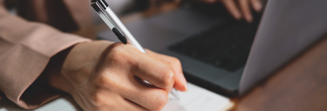 Symbolbild Person arbeitet am PC und schreibt etwas auf